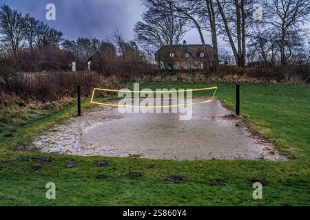 Flooded outdoor sports court with a net, surrounded by grass and countryside in a rural environment during rainy weather. Depicts the effects of natur Stock Photo