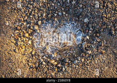 A close-up view of shattered ice on the ground surrounded by pebbles and uneven dirt. Stock Photo