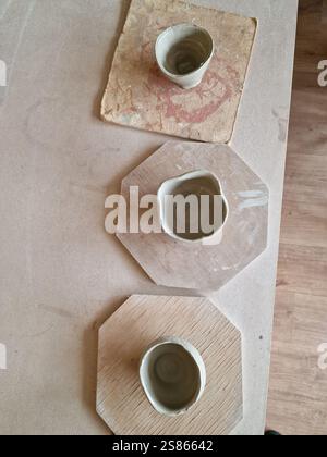 Pottery ceramics workspace with several unfinished clay cups arranged in a row. Raw, unglazed ceramic cups, neutral, rustic, light-colored Stock Photo