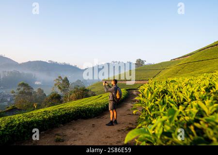 Young man with backpack taking photos of tea plantations in Munnar. Eco tourism in Kerala, India. Stock Photo