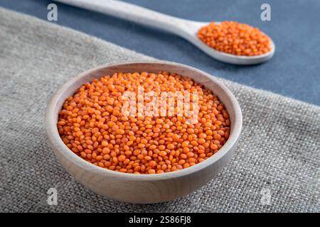 Red lentil grains in a wooden bowl and spoon on a burlap. Top view of dried orange lentils inside the bowl. Stock Photo