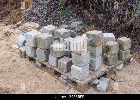 Concrete dumbbells of various weights with iron handles are stacked on the pallet of an outdoor sports field. Stock Photo