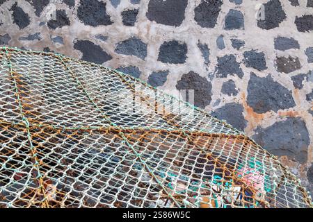 Detail of a green fishing net with rusted parts. Wall made of volcanic stones in the background. Abstract view on the differenct structures. La Santa, Stock Photo