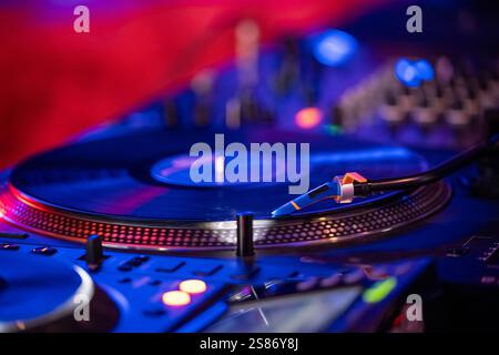 Turntable with vinyl record detail in low light picture. Vinyl record on turntable red and blue background. Detail of turntable needle on record. Stock Photo