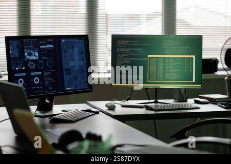Background shot of computers with programs running on screens standing on software developers professional workstation captured against window in office Stock Photo