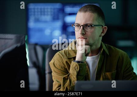 Portrait of thoughtful male software developer reading computer screen with attention solving code problem while working in evening hours in IT company office, copy space Stock Photo