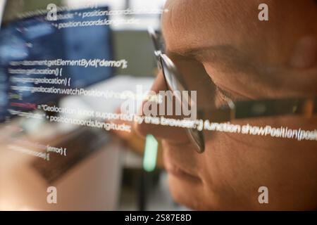Extreme close up shot in warm tones of male programmer wearing glasses reading computer screen with lines of code, double exposure effect, copy space Stock Photo