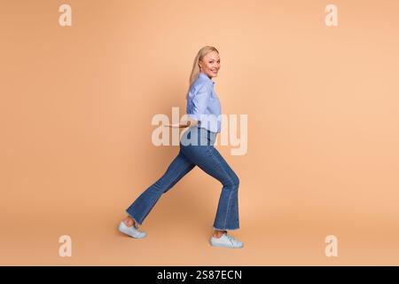 Charming young woman in stylish casual wear smiling joyfully against a beige background, posing gracefully Stock Photo