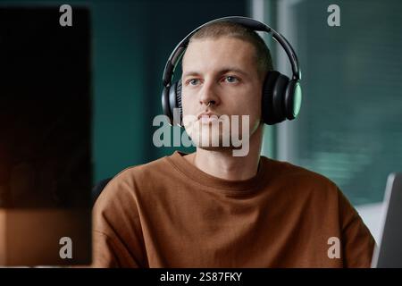 Portrait of senior male IT specialist in headphones working on desktop computer looking intently at screen in tech company office, copy space Stock Photo
