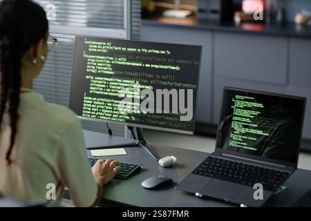 Over shoulder shot of female IT programmer typing source codes on computer using multiple screens working at office workplace Stock Photo