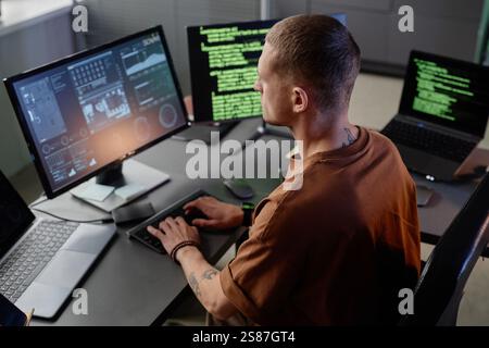 Side view of senior male IT developer typing on keyboard of desktop computer working at desk in modern office space Stock Photo