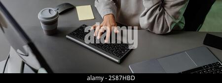 Website header shot of female unrecognizable woman typing on computer keyboard while sitting at working desk with reusable cup at office workplace Stock Photo