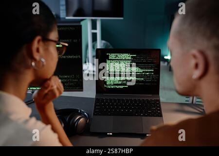Over shoulder shot of female IT programmer looking at laptop screen with code running testing IT product cooperating with male colleague at office workplace Stock Photo