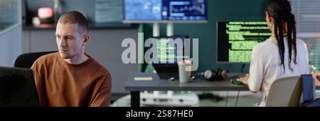 Website header shot of focused male programmer coding on computer at desk working with colleagues in modern IT company office Stock Photo