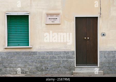 Old house facade with closed roller shutter and plaque on wall, Angera, Italy Stock Photo