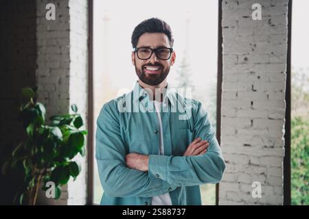 Professional young man standing confidently indoors with crossed arms in a well-lit modern interior Stock Photo