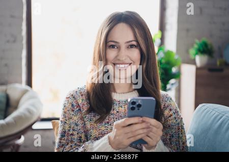 Smiling woman holding a smartphone indoors in a cozy living room with daylight Stock Photo
