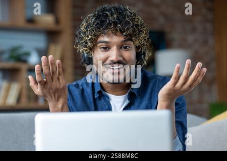 Man working from home remotely, sitting on sofa in living room, freelancer businessman using headset phone and laptop for video call, online meeting and remote conference. Stock Photo