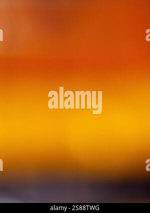 The image is a blurry, out-of-focus shot of a gradient of colours, transitioning from orange-red to a dark brownish-grey. Stock Photo