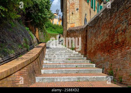 A man walking down long steep stone steps near Via Fontebranda  in Siena  ,Italy Stock Photo