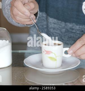 Putting sugar in a cup of coffee on a white plate. Stock Photo