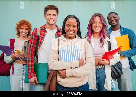 Joyful Group of Multicultural Teenage Students Standing Side by Side with Books and Notebooks, Radiating Positivity and Enthusiasm for Education and Friendship. Young People Against Turquose Backdrop. High quality photo Stock Photo