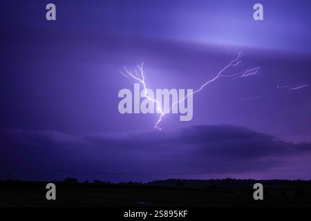 A large bolt of lightning strikes the sky. The sky is dark and stormy. The lightning bolt is very bright and can be seen from a distance Stock Photo