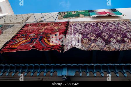 Brightly colored carpets and rugs hang prominently for sale against a building in Essaouira, Morocco, showcasing local craftsmanship. Stock Photo