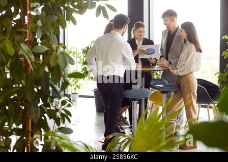 Business team collaborating in office with greenery, discussing charts and financial results. Stock Photo