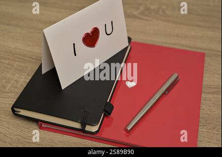 Valentine's Day greeting card romantic letter with red heart and notebooks, pen spread on wooden table. Preparation to celebration Stock Photo