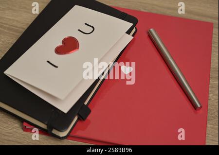 Valentine's Day greeting card romantic letter with red heart and notebooks, pen spread on wooden table. Preparation to celebration Stock Photo