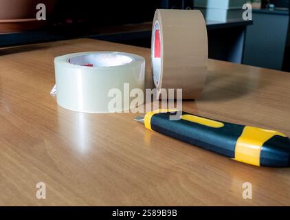 Packing tape and a box cutter are lying on the table Stock Photo