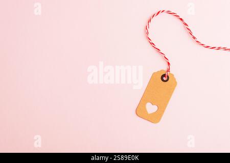 Kraft paper tag with a heart cutout and red twine on a soft pink background. Valentines Day or gift tag designs with copy space. Stock Photo