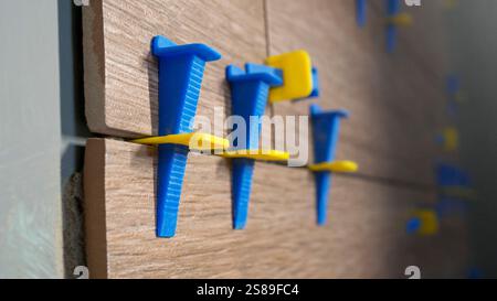 Closeup of blue and yellow plastic tile spacers used for installing tiles during home improvement project. Precise tiling installation for consistent Stock Photo