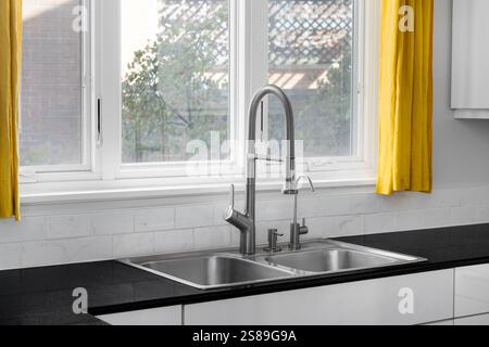 A modern kitchen features a double basin stainless steel sink with a stainless steel faucet, subway tile backsplash, and a black granite countertop. Stock Photo