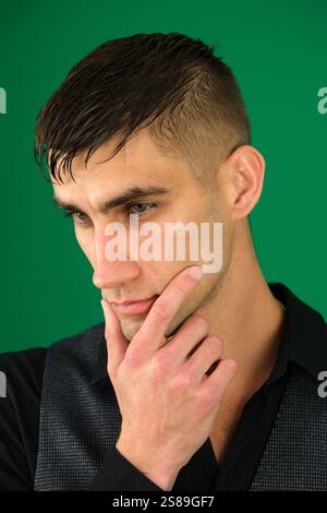 emotions of a handsome man guy on a green background chromakey close-up dark hair young man Stock Photo