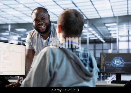 Engineer having fun with colleague at work in data center establishment, making jokes. Team of technicians making each other laugh, bonding in server room, taking break from job Stock Photo