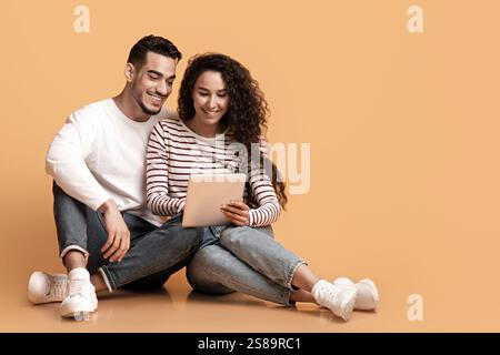 Cheerful Young Arab Couple Browsing Internet On Digital Tablet In Studio Stock Photo