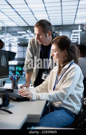 Worker requesting help from senior engineer to fix error in high tech AI data center. Employee in need of aid from IT specialist to repair artificial intelligence supercomputers Stock Photo