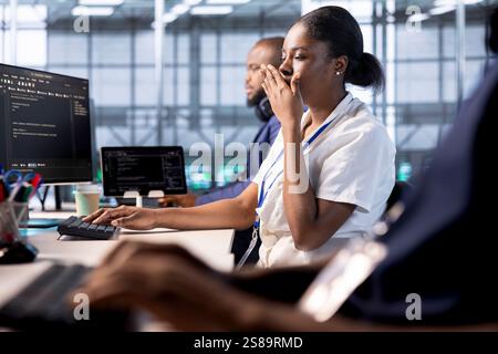 Exhausted developer in data center yawning while using diagnostic tools and system monitoring software. Woman feeling bored while working in server farm, tired of mending equipment Stock Photo