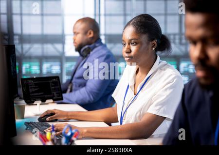 African american developer in data center workspace using diagnostic tools and system monitoring software to identify root cause of errors. Expert working in server hub, mending equipment Stock Photo