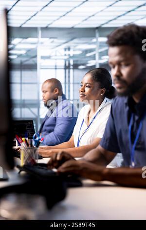 Smiling data center engineer next to colleagues using programming languages to construct algorithms and build applications. Cheerful server hub employee debugging and optimizing code Stock Photo