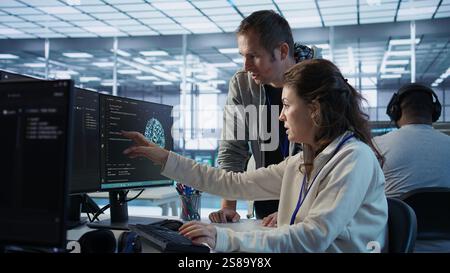 IT team members programming scripts on computer, employing AI machine learning. Software developer and coworker manipulating lines of code for artificial intelligence applications, camera B Stock Photo