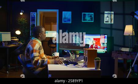 Professional male developer manages neural network at desk, working with AI code on laptop. African american IT expert freelancer developing cyber security, creating secure database. Camera B. Stock Photo
