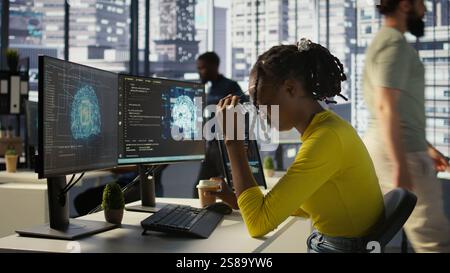 Staff member in office yawning during shift, feeling tired while looking at artificial intelligence software on PC. Exhausted african american AI company employee being sleepy in workspace, camera B Stock Photo
