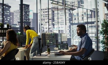 Computer scientist resuming work after strolling in workspace, doing software debugging using PC. Man walking with tablet in office, fixing coding issues using computer, camera B Stock Photo