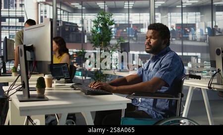 Man with paraplegia conducting code review to fix errors, identifying potential performance and technical issues with software. IT professional with disability in wheelchair optimizing code, camera B Stock Photo
