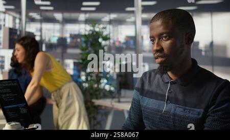 System administrator doing software quality assurance, checking source code on tablet. Close up of african american IT specialist at work inspecting coding on device, looking to fix errors, camera B Stock Photo
