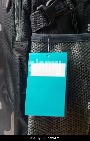 close-up of blank rectangular tag hanging from side pocket of backpack, blue color tag with white space in the center Stock Photo