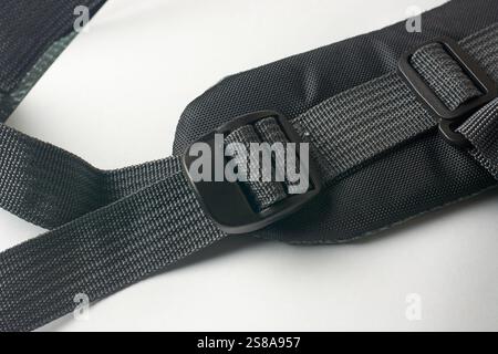 close-up of shoulder strap of black backpack, made of woven fabric with plastic fastened buckle with sliding adjuster, on white surface background Stock Photo